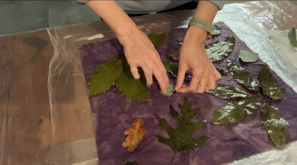 Hands arranging leaves on fabric for eco-printing